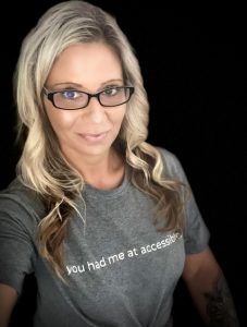 headshot of Dawn Campbell. Blond hair, black framed glasses, grey t-shirt