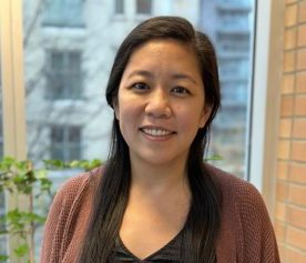 Angela Wu, Executive Director of SWAN Vancouver smiles while standing in front a window in downtown Vancouver.